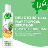A bottle of Wet "Tropical Explosion" Warming Lubricant 🍍 is shown with mango, banana, and pineapple, described as a delicious tropical escape from Wet for sweet, explosive flavor and enhanced oral play.