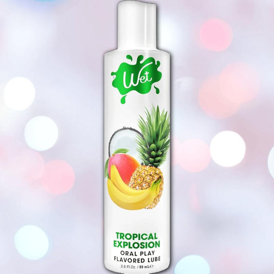 A bottle of Wet "Tropical Explosion" Warming Lubricant 🍍, with vibrant mango, banana, pineapple, and coconut images on the label set against a colorful bokeh background—perfect for a deliciously smooth tropical experience. 1080