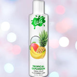 A bottle of Wet "Tropical Explosion" Warming Lubricant 🍍, with vibrant mango, banana, pineapple, and coconut images on the label set against a colorful bokeh background—perfect for a deliciously smooth tropical experience.