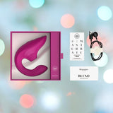 A pink Womanizer Blend Vibrant Air-Pulse Clit Stimulator in its packaging is featured along with G-spot vibrations, a charging cable, a quick start guide, and a card bearing the hashtag "#IMASTURBATE." The background showcases a blurred bokeh effect with soft colors.