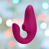 A Womanizer Blend Vibrant Air-Pulse Clit Stimulator Pink, featuring an ergonomic silicone shape with a curved design and G-spot vibrations, is displayed against a softly blurred background illuminated by colorful circular lights.