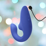 The Womanizer Blend Vibrant Air-Pulse Clit Stimulator Blue, a cutting-edge personal massager featuring three buttons and a charging cable from the Womanizer brand, is shown against a softly blurred backdrop adorned with circular multicolored lights. Experience blended orgasms with its pioneering Air-Pulse Clit Stimulator technology.