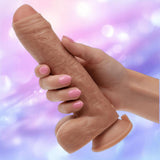 A hand with pink-painted nails holds CalExotics' Working Stiff The Gyrating Bartender, a waterproof vibrator with realistic movement, against a soft pastel background in purple and blue hues.