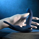 A smooth, white mannequin hand displays the Zero Tolerance By All Means Remote Control Prostate Vibrator, featuring a sleek dark blue, curved design with a metallic accent. It conveys readiness for use against a textured blue background while resting quietly on a wooden surface.