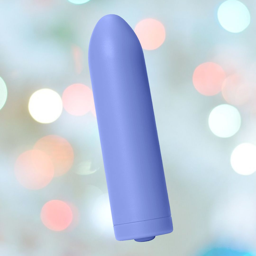 A periwinkle colored, cylindrical Zee Bullet Portable Clitoral Vibrator by Dame with a rounded top and flat base is displayed against a blurred background featuring circular light bokeh in various colors. This smooth and solid USB-rechargeable device by Dame offers three speeds for varied sensations.