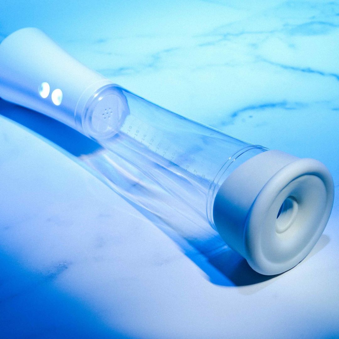 The Zero Tolerance Sucking Good Vibrating Masturbator, a clear cylindrical handheld device with white trim, is positioned on a light blue surface. It includes two buttons for simple control of its suction and vibration features, enhancing its modern allure. The plastic construction exudes a cool, contemporary vibe throughout the scene, making it perfect for those in pursuit of ultimate satisfaction.