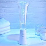 A stylish, modern Zero Tolerance Sucking Good Vibrating Masturbator with a white base rests on a marble surface. Illuminated by a blue light, a vortex can be observed swirling inside. Known for its zero tolerance for leaks, it is positioned among jars and folded towels.