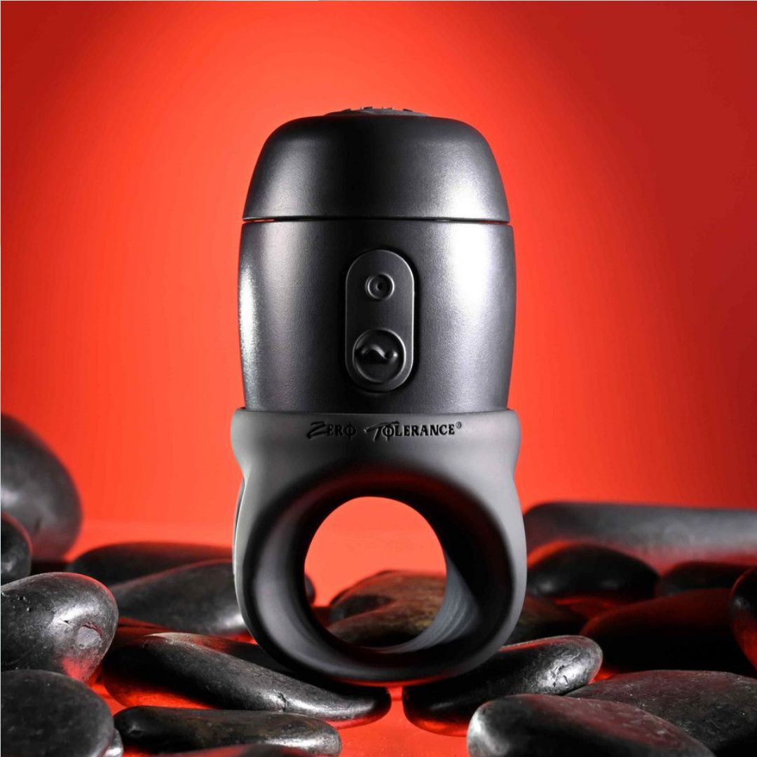 A black and gray Zero Tolerance Wet it Be Lube Dispenser Stroker, featuring a stroker ring that displays the "Zero Tolerance" logo, is set against a red background and surrounded by smooth black stones.