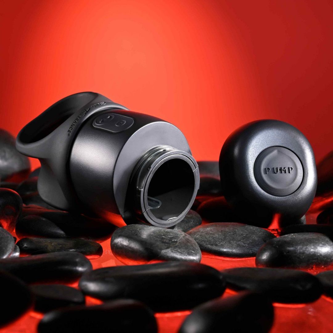 A sleek black bottle of the "Zero Tolerance Wet it Be Lube Dispenser Stroker" rests on a bed of smooth black stones, its cap slightly detached. This enticing display suggests an experience enhanced by this lubricant, all set against a vivid red background that captivates the senses.