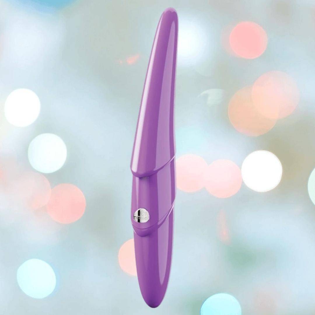 The Zumio S Spirotip Clitoral Stimulator by ZUMIO, INC is shown upright in light purple, featuring a metallic side button and cone-shaped design, against a soft pastel bokeh background, suggesting precise, pressure-sensitive stimulation.