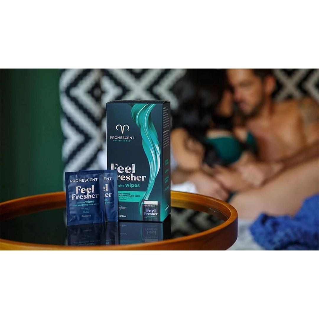 A box and packet of Promescent Before and After Wipes (40 Count) by Promescent sit on a round wooden table, while a blurred couple sits closely together on a bed in the background.