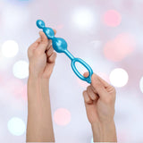 Two hands hold a blue silicone plug from the b-Vibe Butties Bundle by B-Vibe, a premium butt plug kit with 3 sizes and a looped handle, set against a blurred background with pink, white, and blue circular lights.