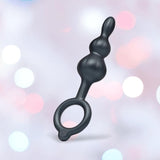 The b-Vibe Butties Bundle: Premium Butt Plug Kit with 3 Sizes by B-Vibe features black silicone plugs with graduated bulbs and a circular handle, shown against a pastel bokeh background of pink, blue, and white light spots.