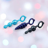 The b-Vibe Butties Bundle by B-Vibe includes three premium silicone butt plugs in blue and black, with ring handles—beaded, spiral, and dual-bulb styles—displayed on a soft pink and white background.