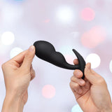 Two hands hold a sleek, black B-Vibe Vibrating Snug Plug RC: Silicone P-Spot Anal Vibrator - Large against a softly blurred, pastel background with circular light spots.
