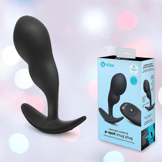 A black B-Vibe Vibrating Snug Plug RC: Silicone P-Spot Anal Vibrator - Large stands upright beside its blue and white box, which shows the plug and remote control, both labeled with the B-Vibe brand. 1080