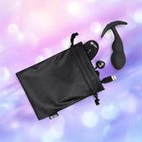 A black drawstring pouch partially open reveals the B-Vibe Vibrating P-Spot Snug Plug RC Large, remote, and USB charging cable by B-Vibe, all resting on a soft purple and blue background—ideal for discreetly storing your essentials.