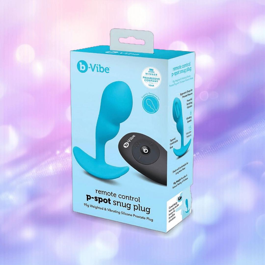 The B-Vibe Vibrating P-Spot Snug Plug RC Small by B-Vibe, a blue remote-controlled prostate stimulator, is featured in its packaging with product images and info, set against a soft purple and pink bokeh background.