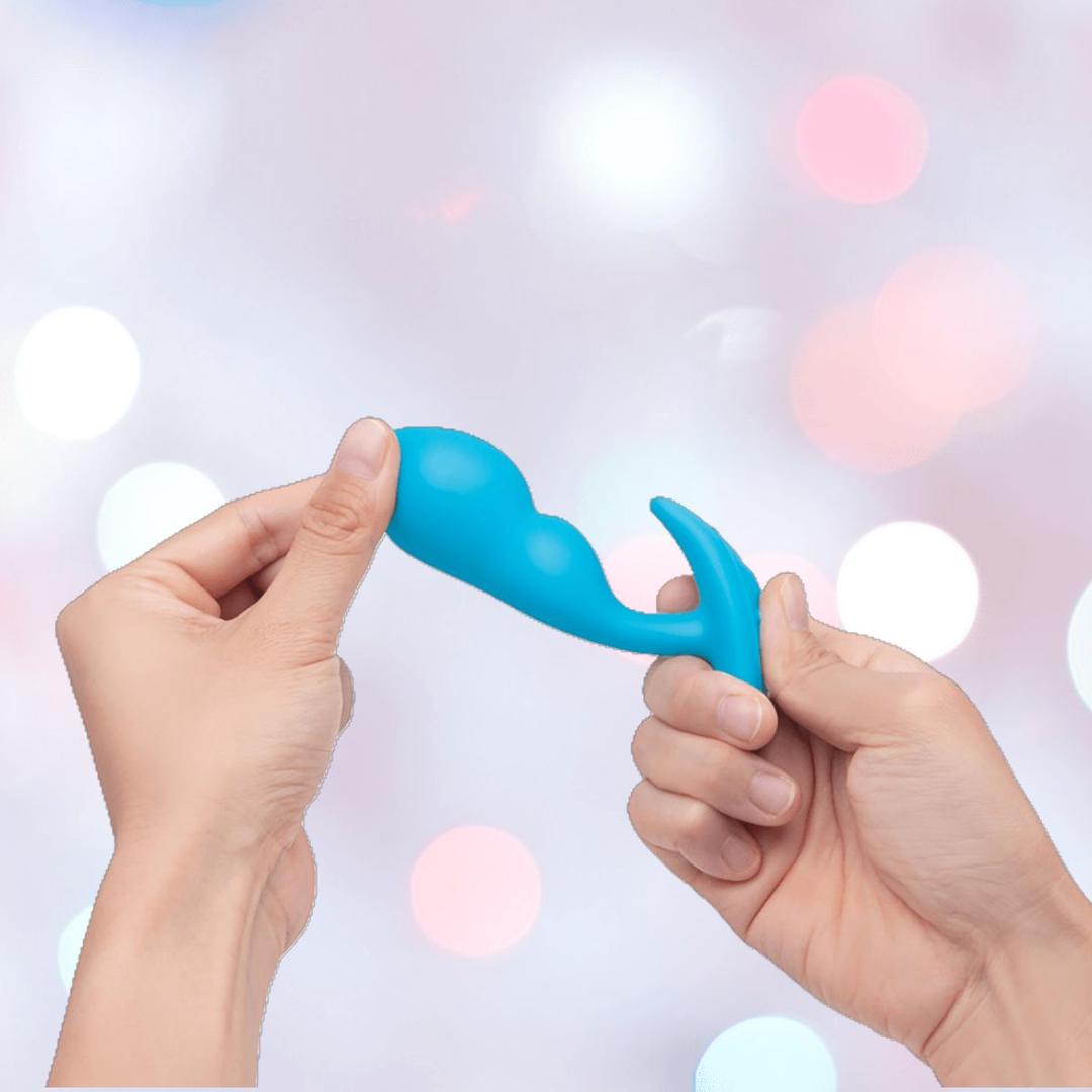 Two hands hold the B-Vibe Vibrating Snug Plug RC: Silicone P-Spot Anal Vibrator - Small against a blurred backdrop, showcasing this B-Vibe remote control anal toy’s sleek, modern design.