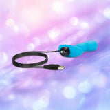 The B-Vibe Vibrating P-Spot Snug Plug RC Small by B-Vibe is a blue silicone butt plug for comfortable prostate stimulation, shown with a USB charging cable on a pink and purple bokeh background.