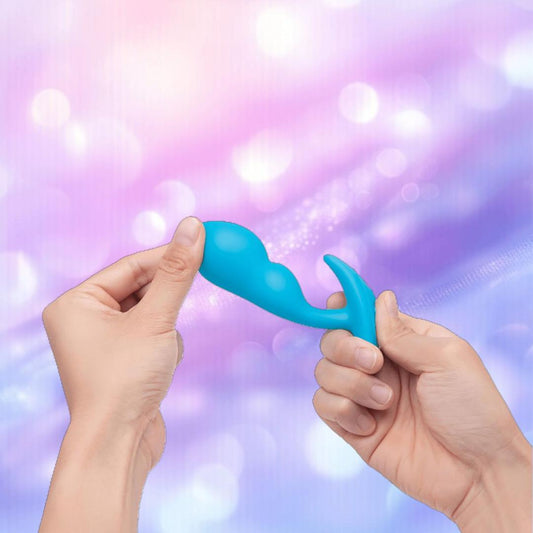 Two hands holding and bending a small, blue B-Vibe Vibrating P-Spot Snug Plug RC Small sex toy against a soft, blurred, purple and pink background. 1080