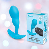 The B-Vibe Vibrating Snug Plug RC: Silicone P-Spot Anal Vibrator - Small is displayed beside its branded box, which features the product image and includes a remote control, all set against a blurred pastel background.
