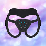 The B-Vibe Every Body Strap-On Harness Set with 6" Silicone Dildo features adjustable black straps and a padded front panel, shown against a soft, pastel pink, purple, and blue blurred background.