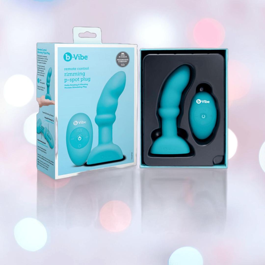 The B-Vibe Remote Control Rimming P-Spot Plug by B-Vibe and its remote are displayed in packaging beside the product box, featuring rotating beads for enhanced prostate stimulation, all set against a softly lit, blurred background.