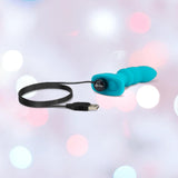 The B-Vibe Remote Control Rimming P-Spot Plug by B-Vibe is a blue, silicone USB-rechargeable prostate vibrator with flexible rotating beads and an attached charging cable, shown on a pastel background with bokeh light effects.
