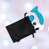 A black drawstring pouch with the B-Vibe Remote Control Rimming P-Spot Plug, remote, and USB charging cable—featuring rotating beads for prostate stimulation—is partially visible on a softly blurred pastel background.