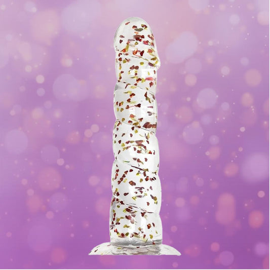 The Icon Brands Glittergasm Dong - Red and Orange Swirl 8" stands upright against a purple background with bokeh light effects, showcasing its clear, textured design containing small flower petals. 1080