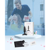 A promotional image features a man playfully covering a woman's eyes as she smiles, holding a gift box. In the foreground, there's a product display of the Lovense Hush 2 Vibrating Butt Plug - XS by Lovense, complete with its packaging, charging cable, and pouch on an elegant white platform.