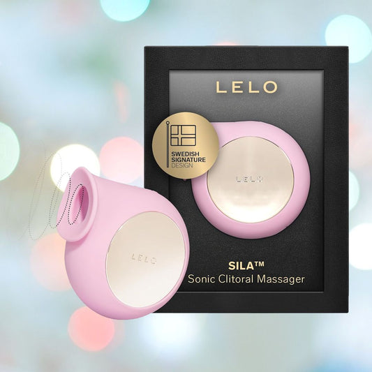 A pink LELO SILA Air Suction Clitoral Massager, made from extra-soft silicone and featuring a gold accent, is showcased alongside its black packaging. The packaging highlights a gold badge stating "Swedish Signature Design," surrounded by a gentle blur of blue and gray tones. 1080