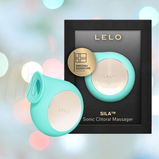 An aqua LELO SILA Air Suction Clit Massager is pictured in front of its black and gold packaging. The device and packaging both feature the LELO logo, with a gold badge highlighting its Swedish signature design. Known for clitoral stimulation using air suction waves, it also boasts a waterproof design. The background has a soft, blurred bokeh effect. 1080