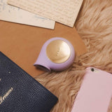 A LELO SILA Air Suction Clit Massager in Lilac is placed on a soft, beige surface alongside a closed book, a pink smartphone, and handwritten letters. The scene exudes a cozy, vintage aesthetic as the device promises soothing clitoral stimulation with its gentle sonic waves.