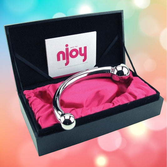 A shiny, curved Njoy Pure Wand Non-Vibrating Metal G-Spot and P-Spot Massager with a spherical end is displayed inside an open black box, resting on a pink satin-like lining. The box has a card with the word "Njoy" on it. The background is colorful and blurred with pastel hues. 1080