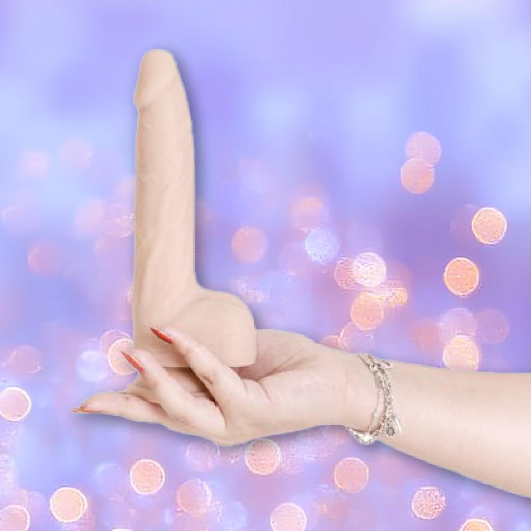 A hand with red-painted nails and a silver bracelet holds the BMS Naked Addiction Thrusting Dong - Vanilla 8.5", a realistic IncrediFeel silicone dildo, against a blurred purple background with bokeh lights.