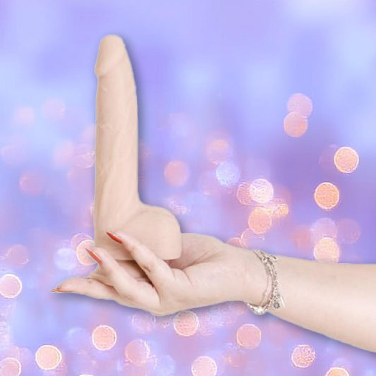 A hand with red-painted nails and a silver bracelet holds the BMS Naked Addiction Thrusting Dong - Vanilla 8.5", a realistic IncrediFeel silicone dildo, against a blurred purple background with bokeh lights. 1080