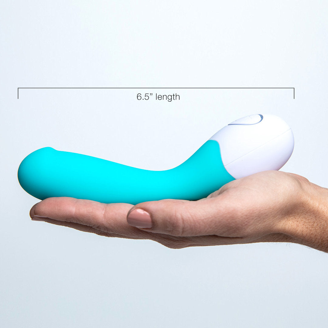 A hand holding the OhMiBod Lovelife Cuddle G-Spot Vibrator in turquoise against a light grey background. The 6.5-inch device, featuring a sleek and ergonomic design for targeted sensations, has a visible button on the white part.