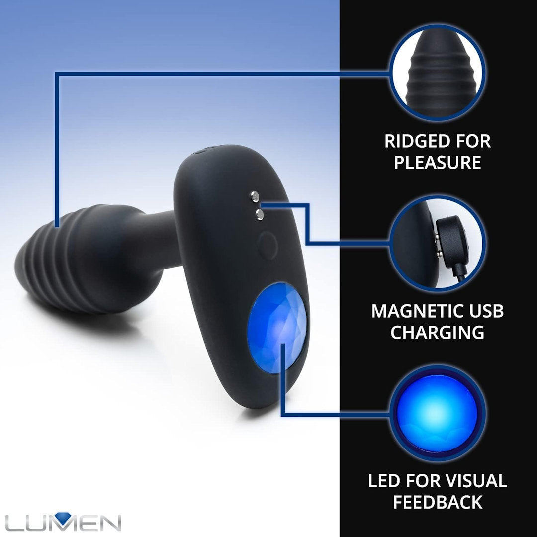 The OhMiBod Lumen Vibrating Butt Plug, a sleek black device with a ridged texture, boasts three standout features: "Ridged for pleasure," "Magnetic USB charging," and "LED brilliance for visual feedback." This innovative product has a wide top with an LED light and a narrow base, featuring the brand name "LUMEN" prominently displayed in the bottom left corner.