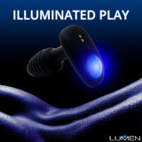 A sleek, black silicone personal massager featuring a radiant blue light at its center is set against a dark, misty blue background. The words "ILLUMINATED PLAY" are prominently displayed at the top, while the product name "OhMiBod Lumen Vibrating Butt Plug" by OhMiBod appears in the bottom right corner.