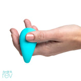 Against a white background, a hand holds a small, turquoise, teardrop-shaped object with painted light pink nails highlighting its smooth surface. Made from body-safe silicone, this personal use finger vibe showcases the "OhMiBod Lovelife Rev" logo in the corner.