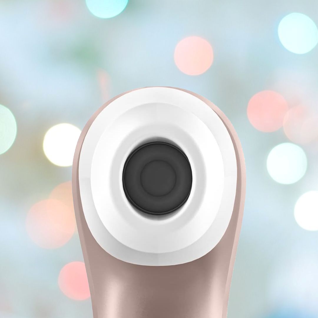 Close-up of a circular, modern device resembling the Satisfyer Pro 2 Air Pulse Clitoral Stimulator by Satisfyer, featuring a central dark lens, set against a blurred background with colorful bokeh lights.