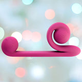 A pink, S-shaped abstract sculpture with a smooth surface. The background is softly blurred with pastel bokeh lights. The sculpture, reminiscent of the Snail Vibe Dual-Motor Thrusting Vibrator (Pink) by Snail Vibe, features circular ends marked with an engraved logo, hinting at clitoral stimulation and dual stimulation functionalities.