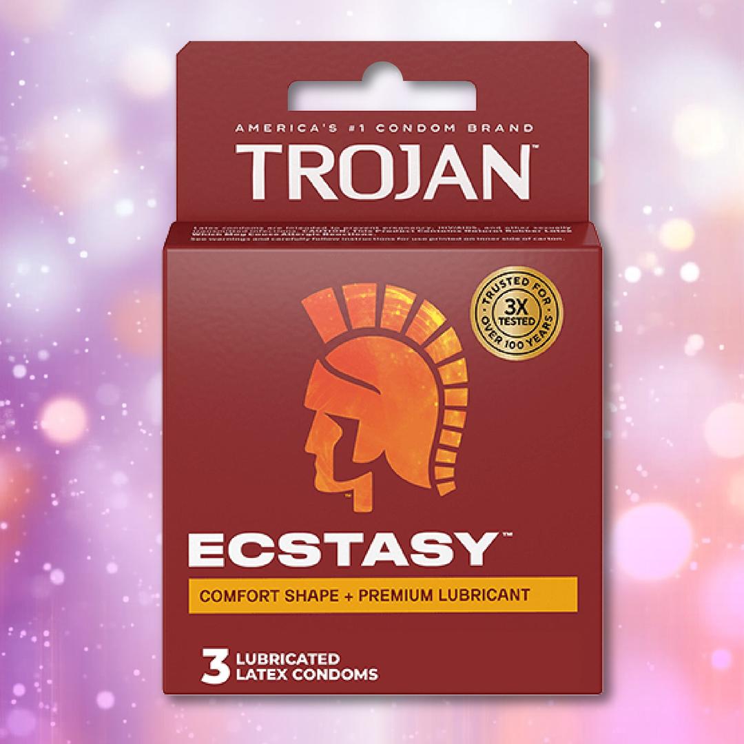 A box of Trojan Ultra Ribbed Ecstasy Condoms by Trojan, featuring a red and orange design, appears against a pink and purple bokeh background. The packaging contains 3 premium lubricated condoms and displays the Trojan helmet logo.