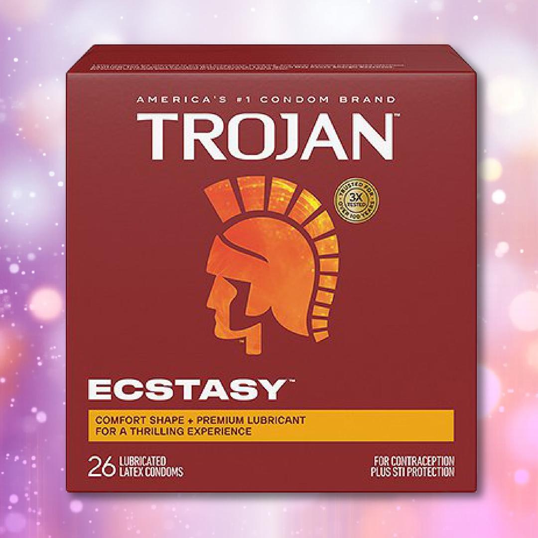 A 26-count box of Trojan Ultra Ribbed Ecstasy Condoms by Trojan features a red background, gold Trojan helmet logo, and text highlighting comfort shape and premium lubrication. The blurred background glows with purple and pink lights.