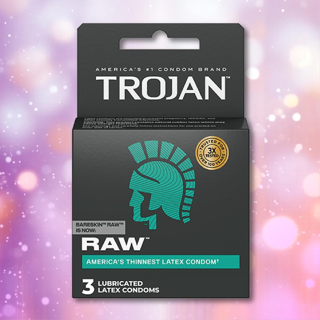 A box of Trojan Raw Ultra-Thin Condoms by Trojan, featuring teal and white text and the Trojan helmet logo, rests against a blurred pastel background. The box contains 3 lubricated condoms.