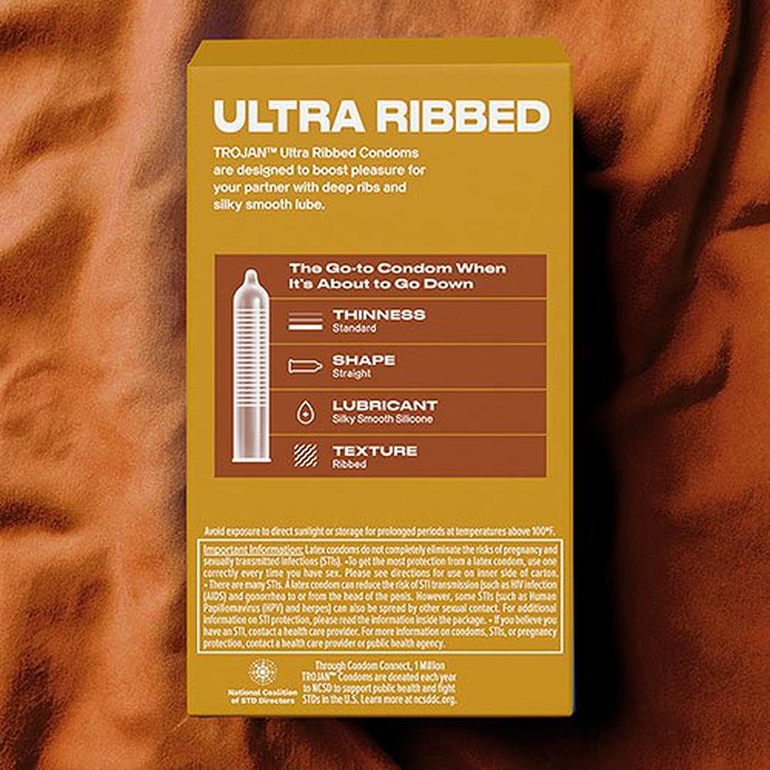 A yellow box of Trojan Ultra Ribbed Condoms by Trojan rests on brown satin, highlighting its thin, straight-shaped, lubricated latex condoms with a silky smooth feel and ribbed texture. A condom diagram is also displayed for clarity.