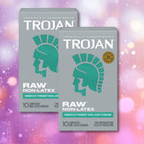 Two boxes of Trojan Raw Non-Latex Condoms by Trojan are displayed against a pink and purple bokeh background. The gray packaging with teal accents features the Spartan helmet logo, emphasizing that these premium condoms offer a latex-free polyurethane option.
