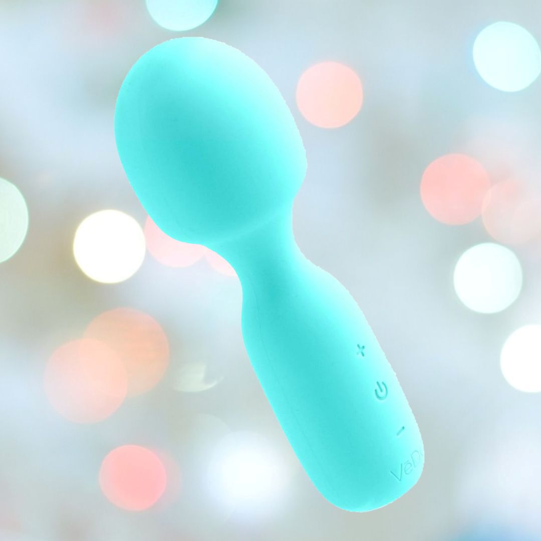 The VeDO WINI Mini Vibrator Wand in Turquoise is a rechargeable massager featuring a sleek, smooth design with a rounded head. The handle is equipped with three buttons: a plus sign, a power symbol, and a minus sign. With 10 vibration modes to choose from, this wand stands out against an abstract bokeh background of white, pink, and blue hues.